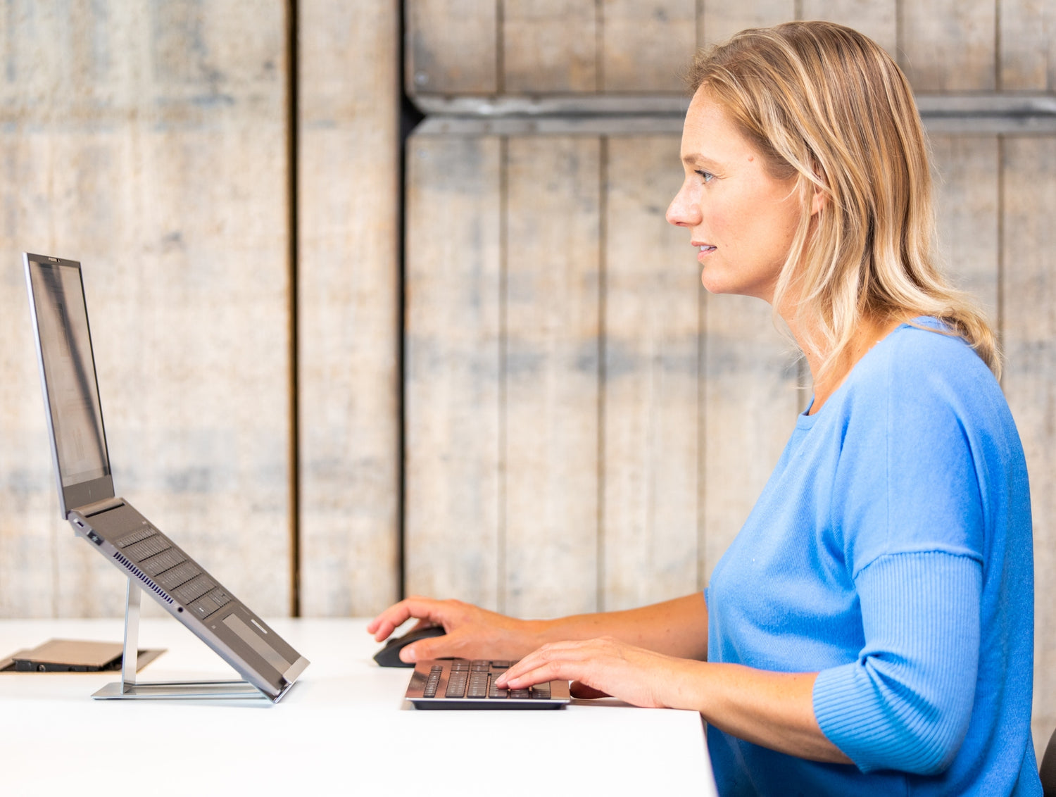 Vrouw zit met correcte houding achter OviStand Max laptopstandaard